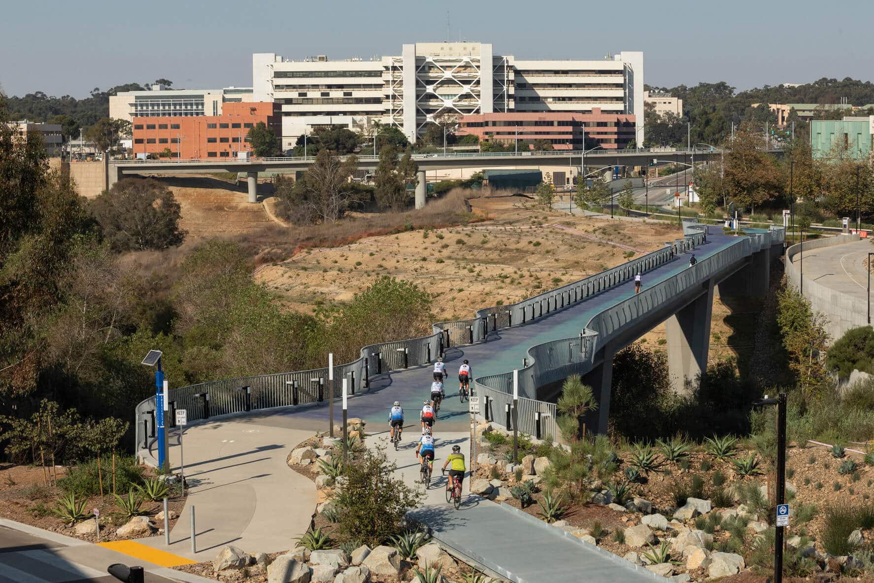 Pedestrians walking across the UCSD pedestrian bridge leading to UCSD campus